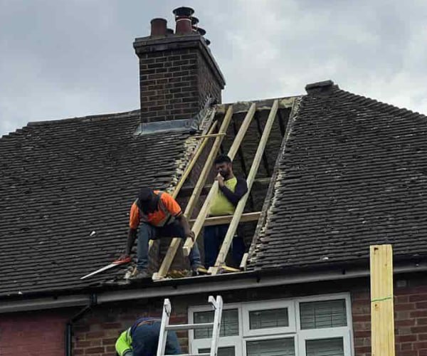 This is a photo of a roof repair being carried out. A section of the roof has been stripped and two roofers are replacing the rafters. Works being carried out by FP Roofing Sandy